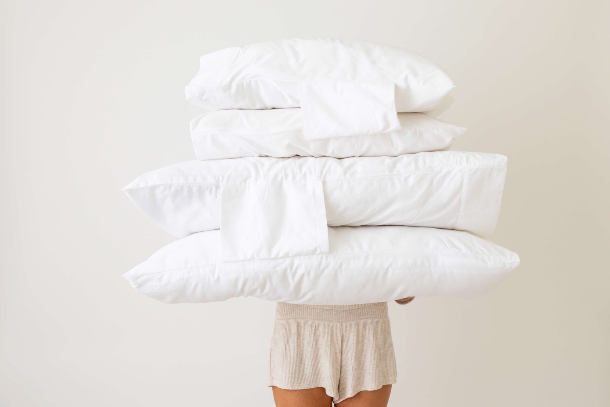 A stack of pillows and folded Everside Dual Pillowcases held in front of a person